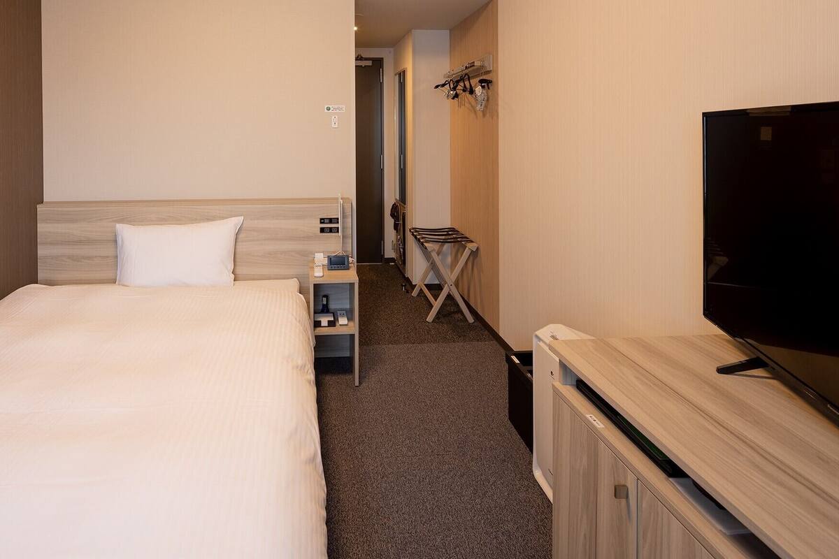 Habitación de hotel con cama, televisor, una mesita y un zapatero.