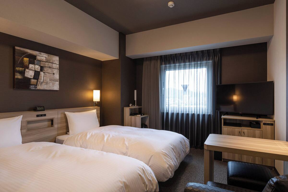 Habitación de hotel con dos camas, un escritorio, un televisor y un cuadro en la pared.