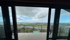 A view from a balcony with a railing, overlooking a landscape with a body of water and distant buildings. - The Wood House Loft (Ngāruawāhia)