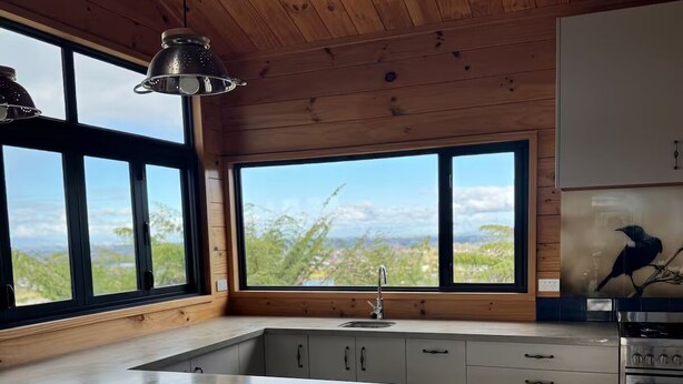 A modern kitchen with a large island, wooden ceiling, and large windows offering a view of the outdoors. - The Wood House Loft (Ngāruawāhia)