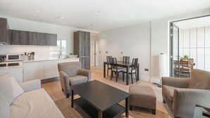 A modern living room with a dining area, a kitchen, and a sliding glass door leading to a balcony. - GuestReady - Modern 1BR by Battersea Park (London)