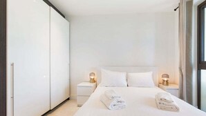 A modern hotel room with a large bed, white linens, two bedside lamps, and a view through a window. - GuestReady - Modern 1BR by Battersea Park (London)