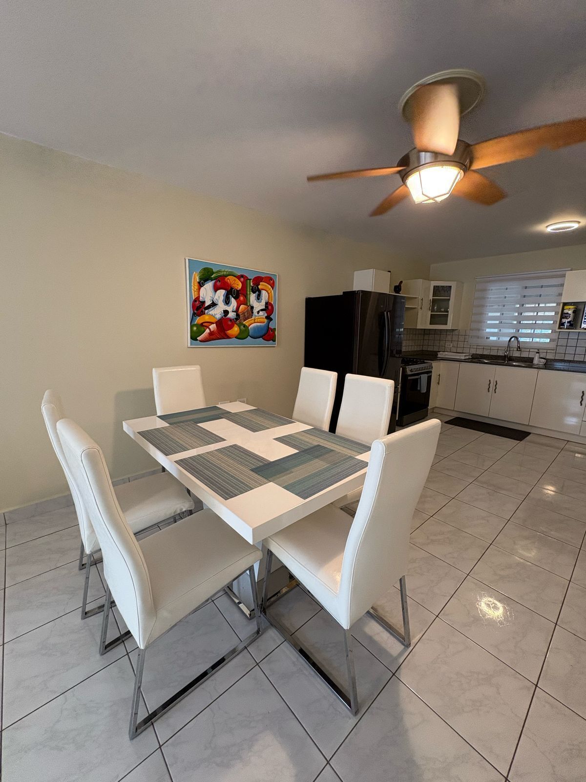 A modern kitchen with white cabinets, a black refrigerator, and a dining area with a white table and chairs.