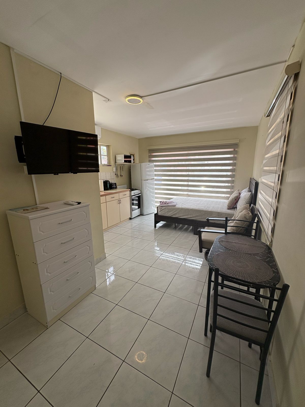 A compact living space with a kitchenette, a bed, a TV mounted on the wall, and a small dining area.