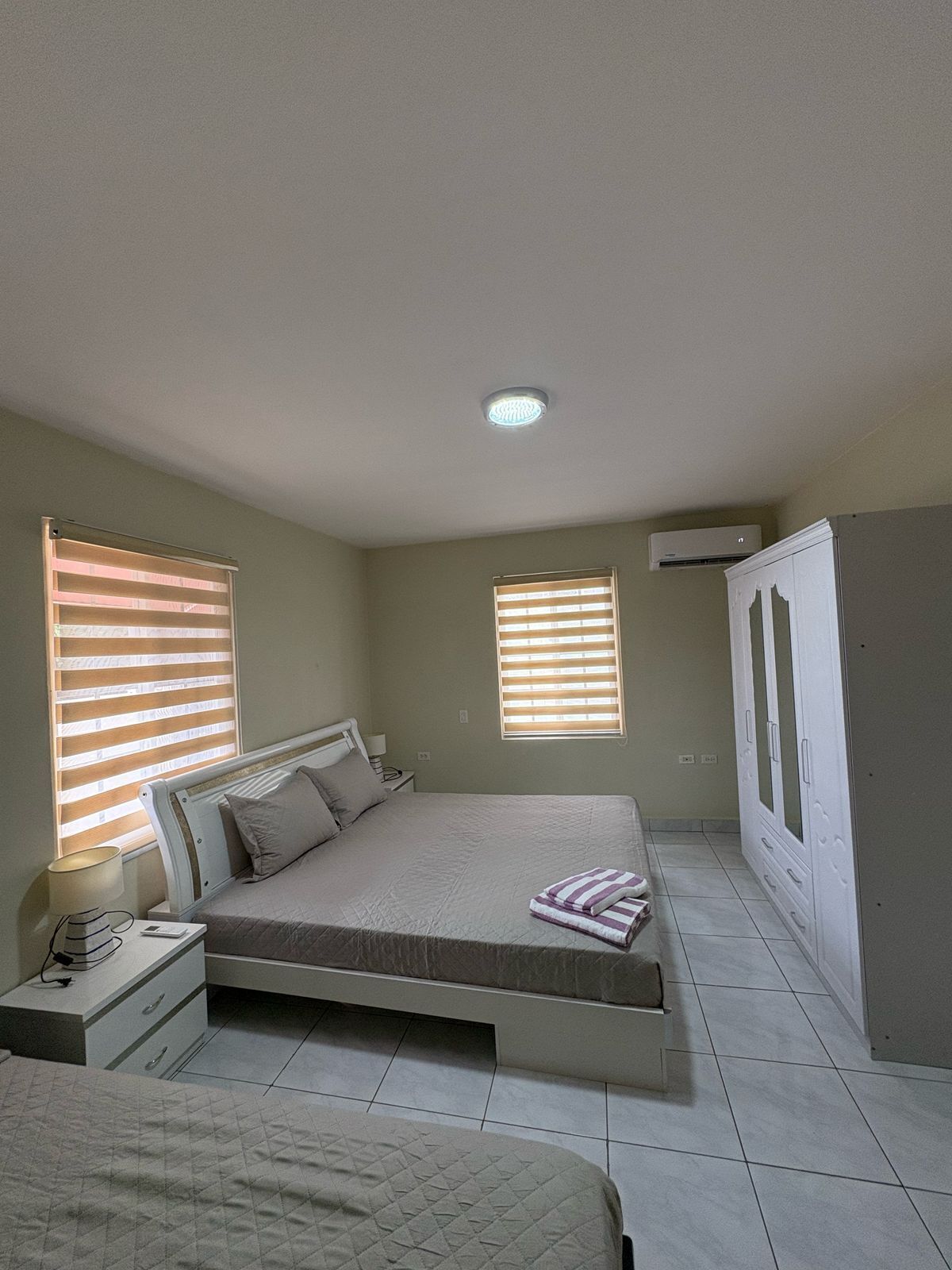 A bedroom with a bed, bedside tables, a wardrobe, and two windows with blinds.