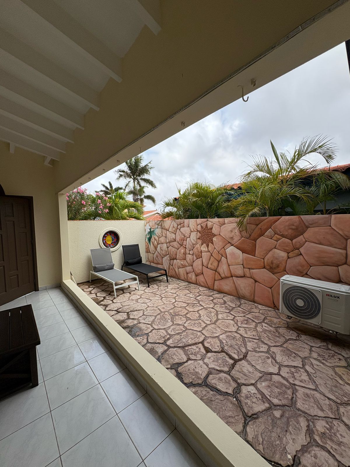 An outdoor patio area with a stone wall, two lounge chairs, a small table, and an air conditioning unit.