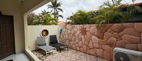 An outdoor patio area with a stone wall, two lounge chairs, a small table, and an air conditioning unit.