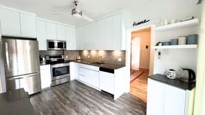 Una cocina moderna con armarios blancos, electrodomésticos de acero inoxidable, encimera negra y suelo de madera.