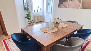 Un comedor con una mesa de madera, sillas azules y grises, un tapete con estampado rojo y blanco, y una araña.
