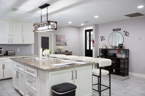 A modern kitchen with white cabinets, a granite countertop, and a bar area with stools. - Westbury Getaway- PoolTable, Patio, &Grill- 4BD/3.5BA (Houston)