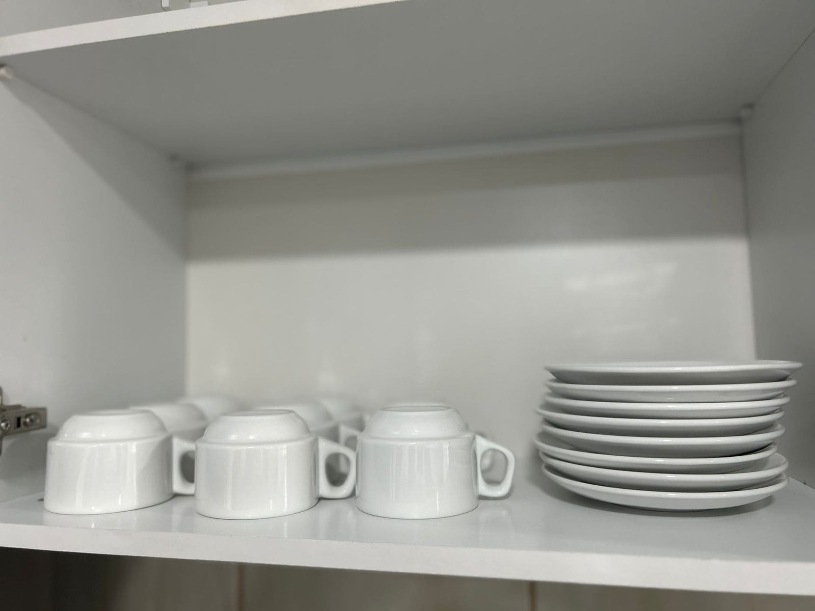 A white shelf with white mugs and stacked plates.
