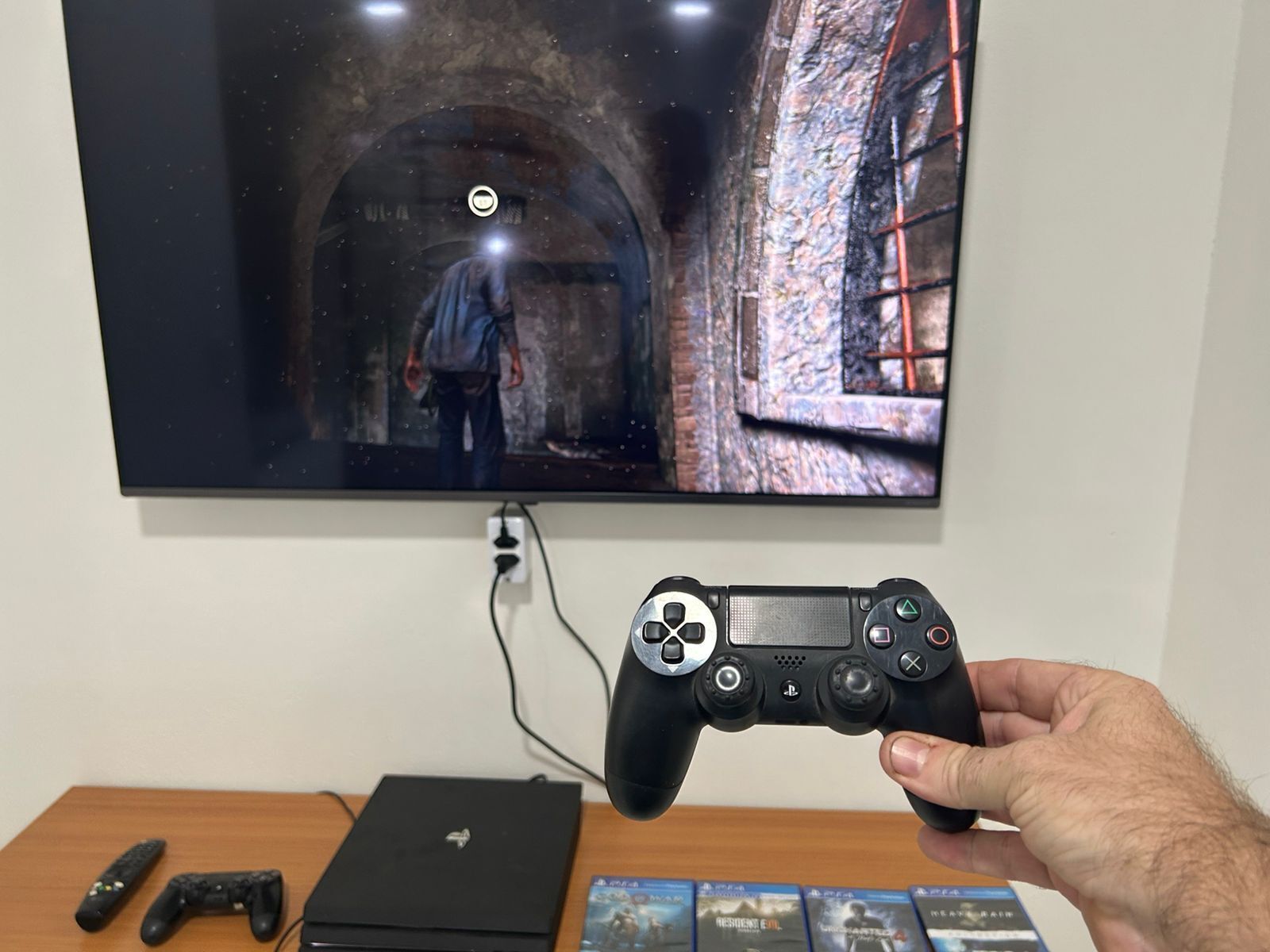 A person holding a PlayStation controller in front of a TV displaying a game scene.