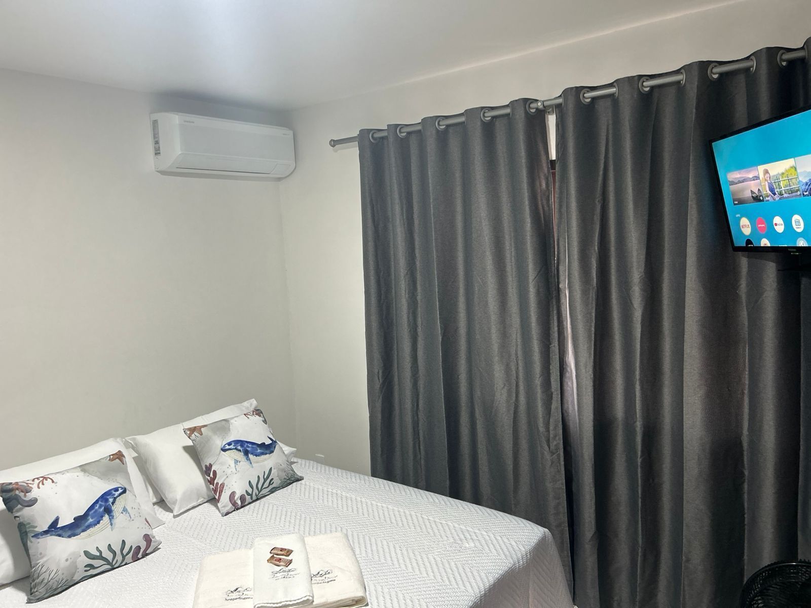 Habitación de hotel con cama, televisor de pantalla plana, cortinas grises y aire acondicionado instalado en la pared.