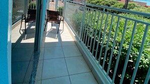A balcony with a tiled floor, a metal railing, and a view of a street with buildings and greenery.