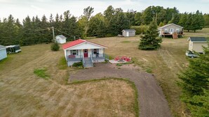 A single-story house with a red roof and a porch, surrounded by a yard and trees. - Charming Cavendish-Area Cottage with River Views—Peaceful PEI Retreat (Prince Edward Island)