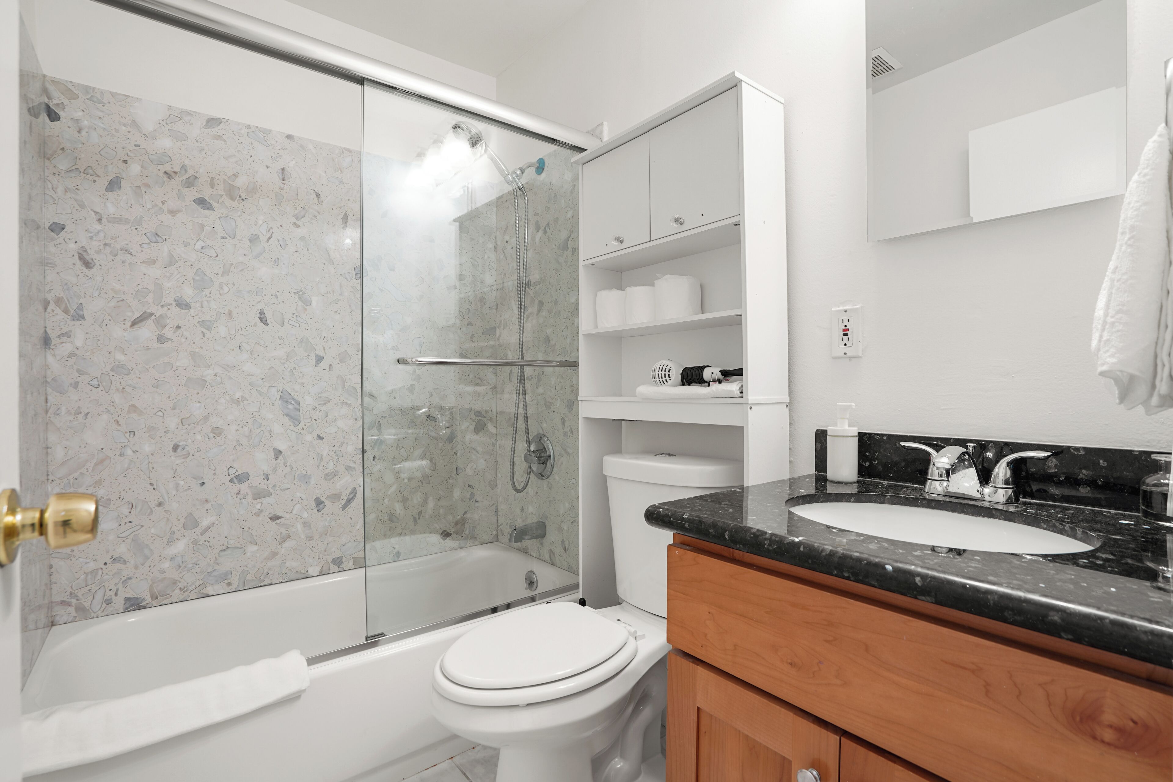 Un baño moderno con cabina de ducha de vidrio, inodoro blanco, lavamanos de encimera negra y armarios de madera.
