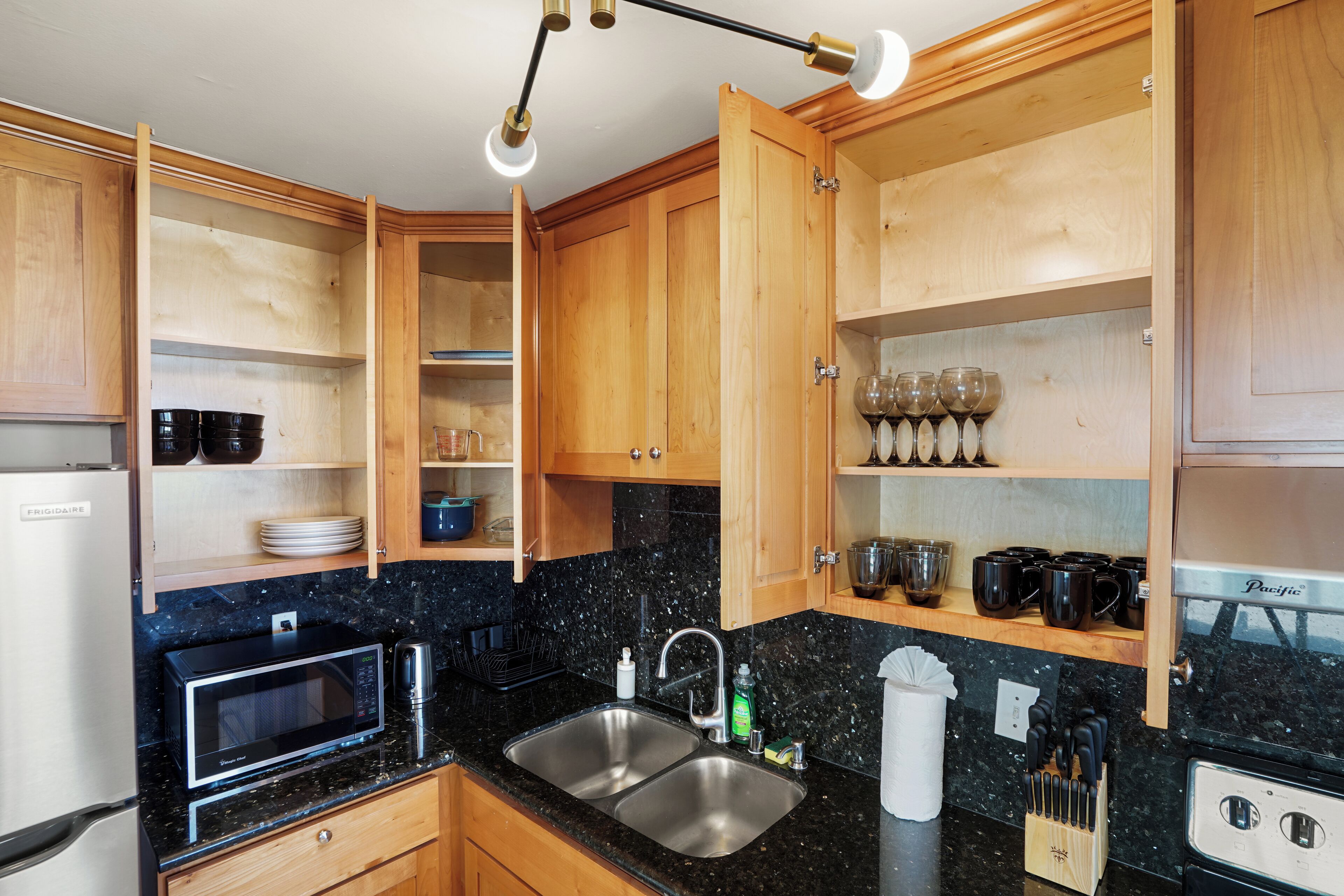 A compact kitchen with wooden cabinets, a black granite countertop, a stainless steel sink, a microwave, and a coffee maker.
