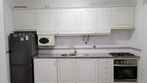 Una cocina con armarios blancos, un refrigerador, un microondas, un fregadero y una estufa.