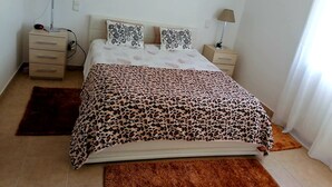 Un dormitorio con cama, dos mesitas de noche, una lámpara sobre cada una, un tapete y una ventana con cortinas.