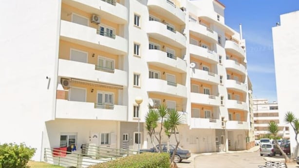 Un edificio residencial de varios pisos con balcones, zona de estacionamiento y cielo despejado.