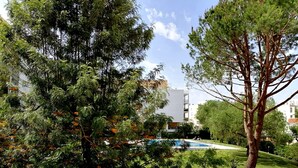 Una zona de piscina rodeada de árboles y un edificio al fondo.
