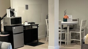 Een kleine keuken met een magnetron, koelkast en koffiezetapparaat. Er is een eethoek met een tafel en stoelen.