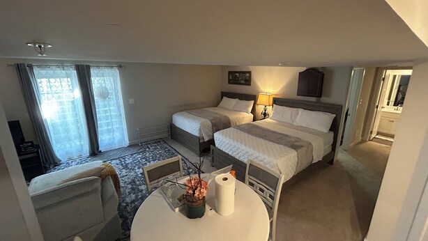 Een hotelkamer met twee bedden, een tafeltje met een bloevas, een stoel en uitzicht buiten door een raam met gordijnen.