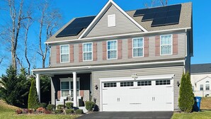 Een huis met twee verdiepingen, een overdekte veranda, een garage en zonnepanelen op het dak.