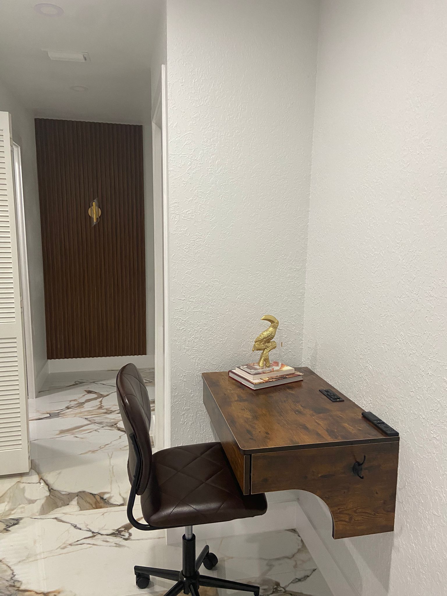 A corner office with a wooden desk, a black office chair, and a decorative golden bird statue.
