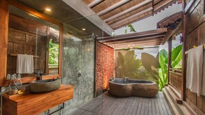 Et moderne badeværelse med vask i sten, bruseafskærmning i glas og en træterrasse med jacuzzi.