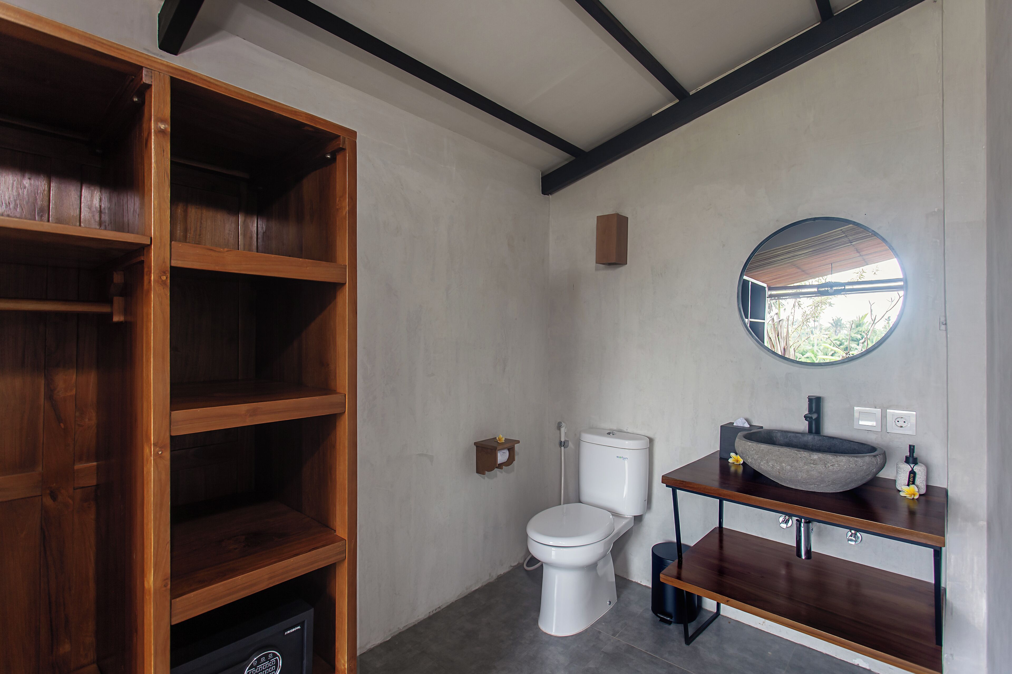 A modern bathroom with a wooden shelving unit, a round mirror, a vessel sink, and a toilet.