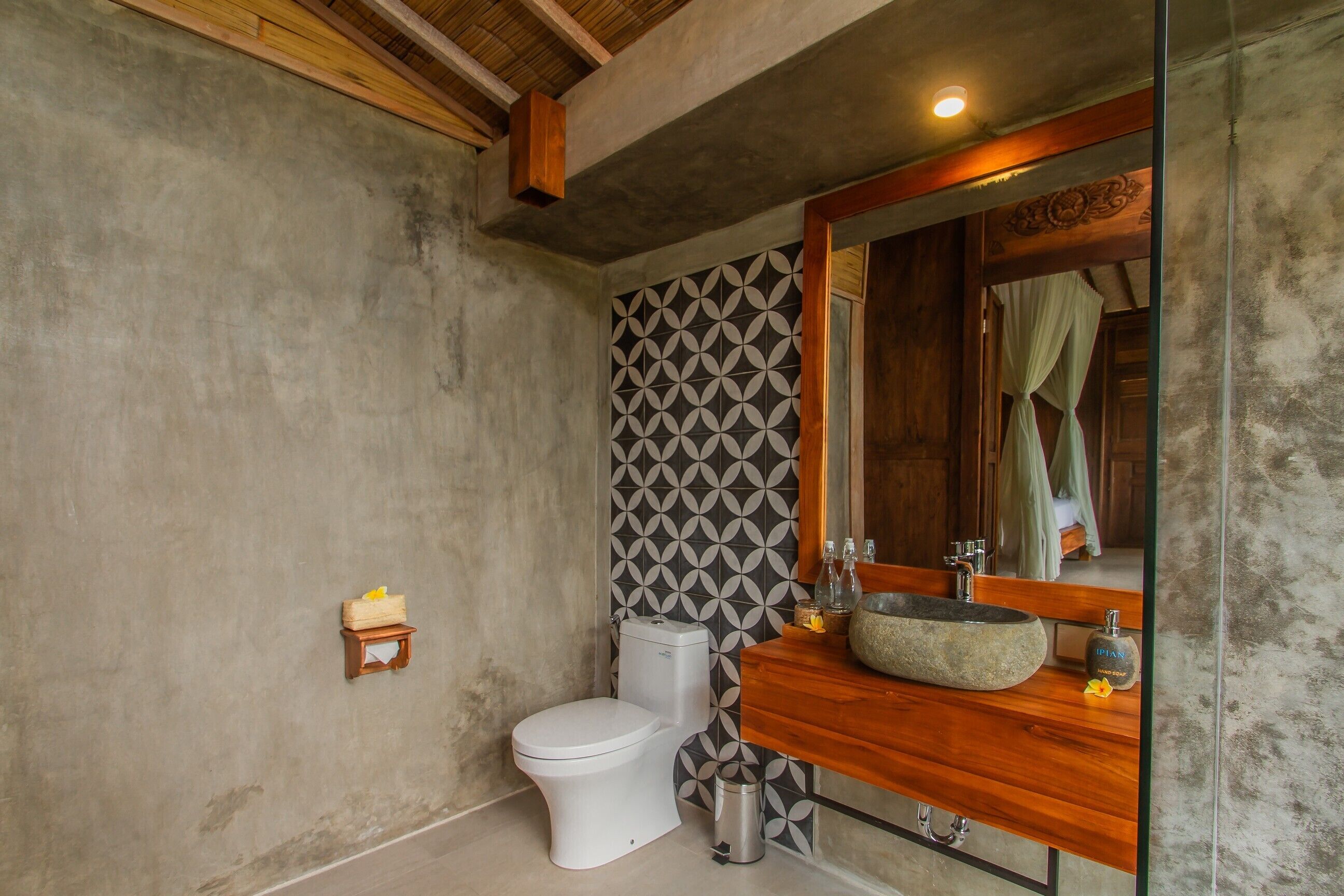 Un baño con inodoro blanco, lavamanos de piedra y espejo con marco de madera.