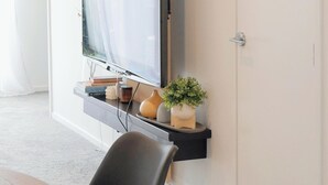 A modern room with a flat-screen TV mounted on a wall, a wooden door, a staircase, and a small potted plant. - A Quiet Modern / Brand New Gem (Lower Hutt)