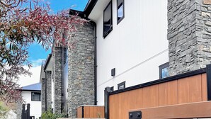 A modern building with stone and wood exterior, numbered mailboxes, and a gated entrance. - A Quiet Modern / Brand New Gem (Lower Hutt)