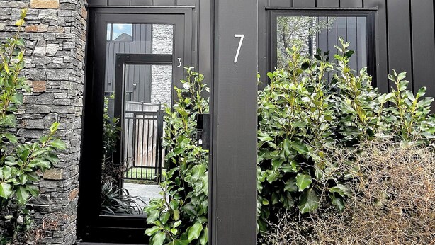 A modern house with a stone exterior, a black door with the number 7, and a small garden with bushes. - A Quiet Modern / Brand New Gem (Lower Hutt)
