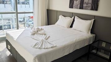Relax in a spacious room with a large bed, a window offering a view of the city, and a black and white artwork above.