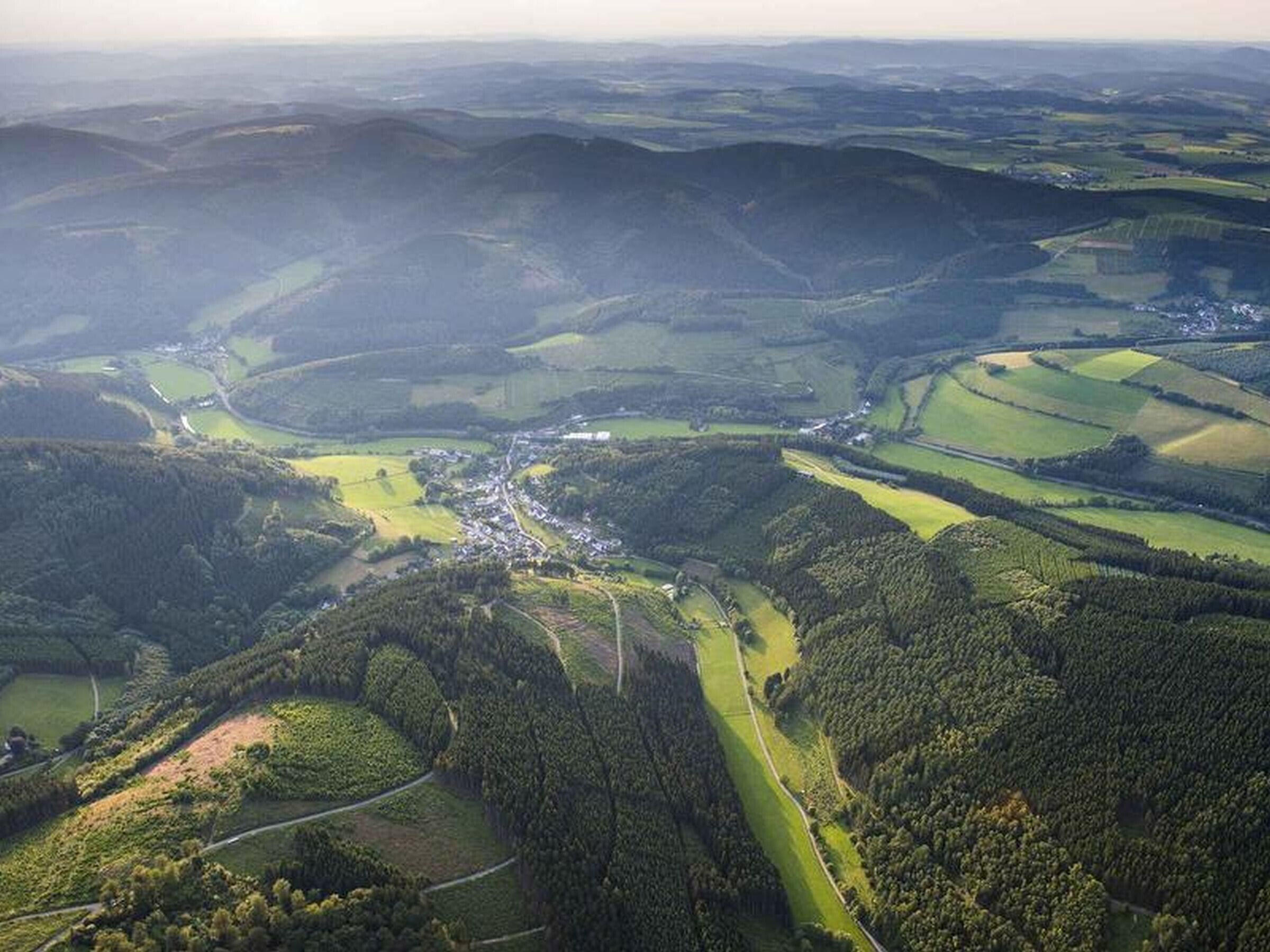 Une vue aérienne d’un paysage rural, avec des collines ondulantes, des champs et un petit village.