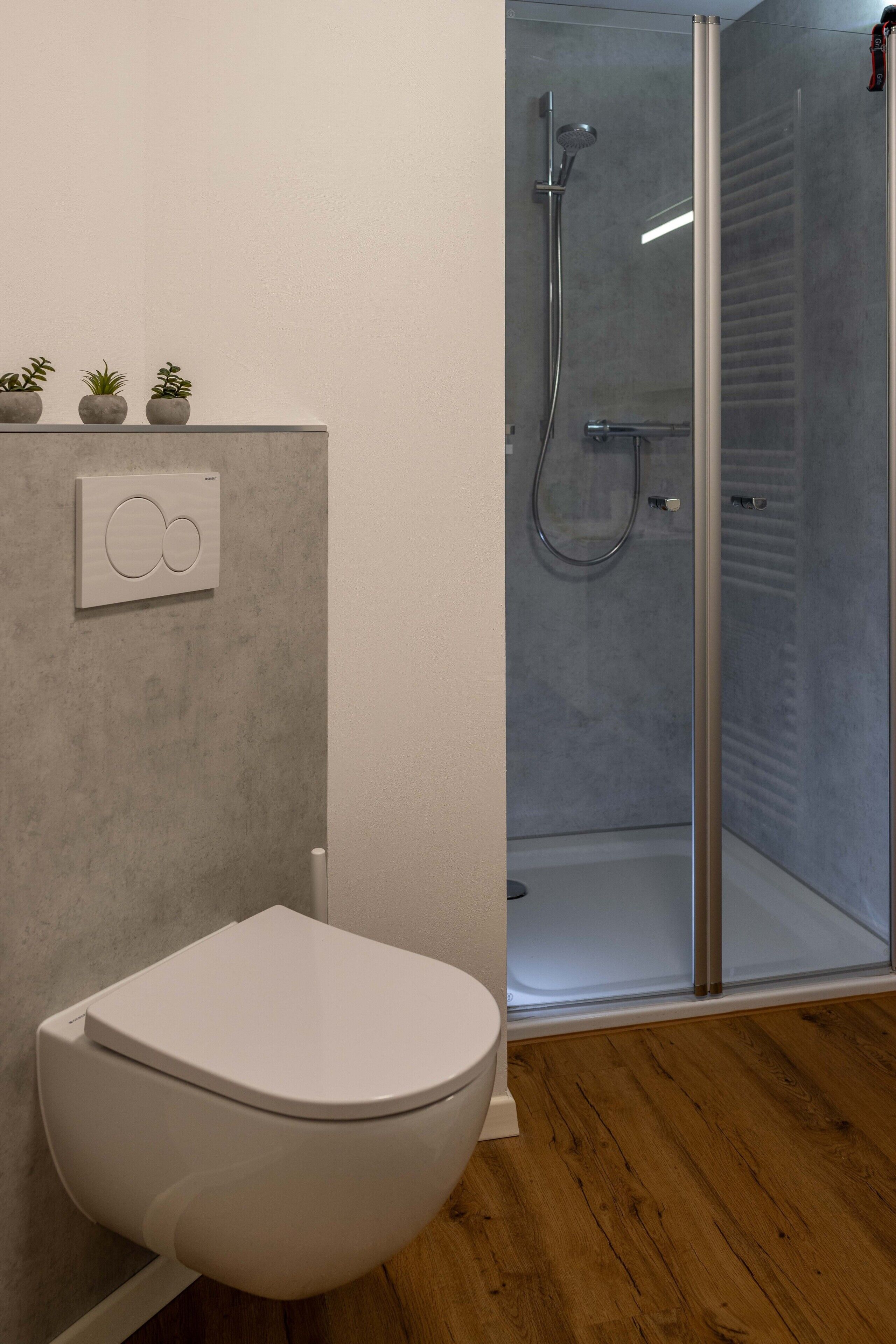 A bathroom with a toilet, a shower enclosure, and a wall-mounted control panel.