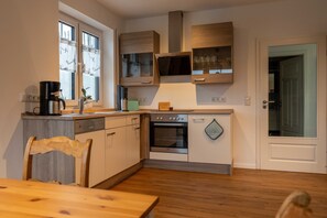 A compact kitchen with a dishwasher, oven, and a microwave. There is a wooden dining table and chairs.