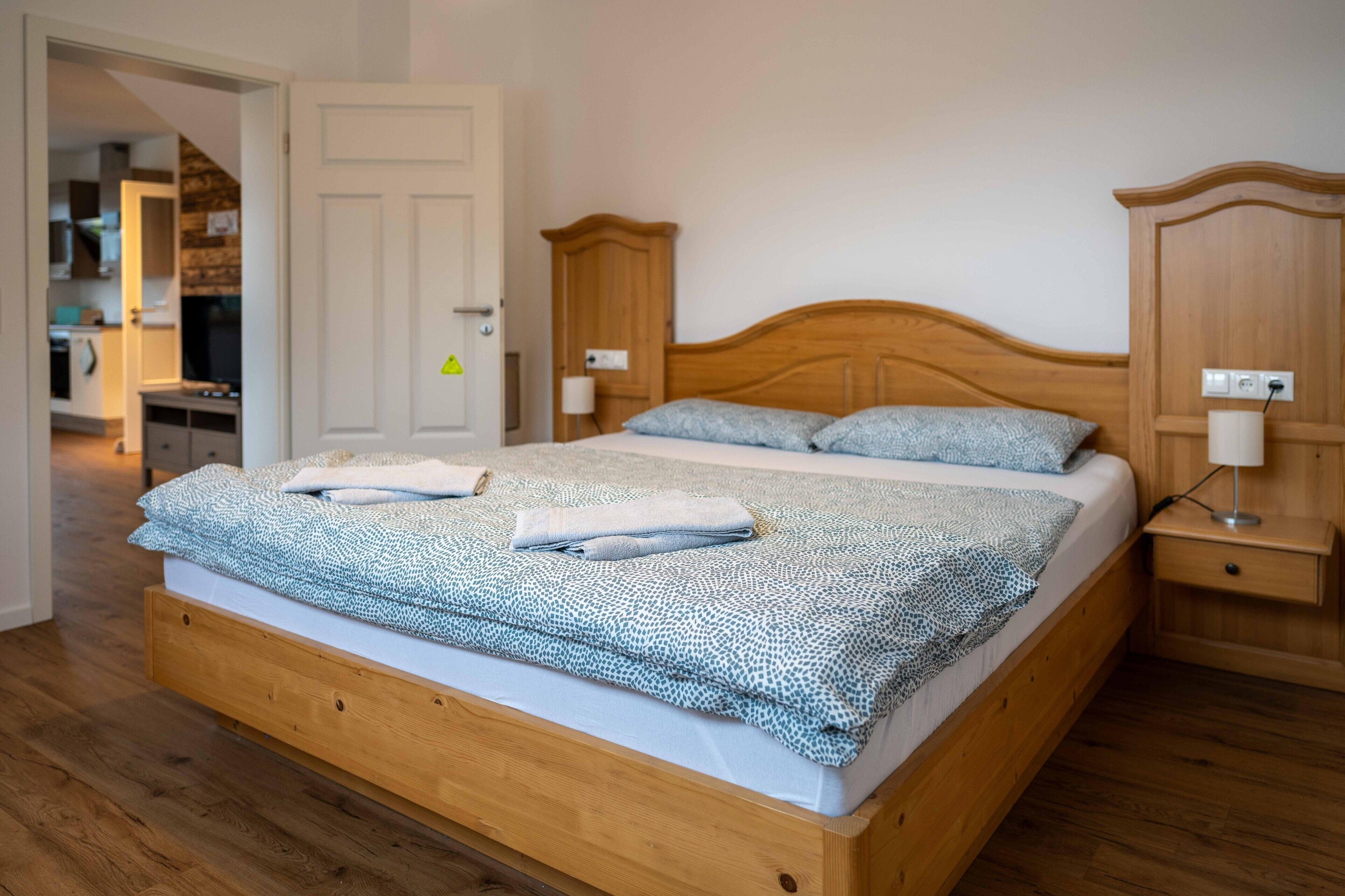 A wooden bed with a patterned bedspread, a bedside table, and a nightstand with a lamp.