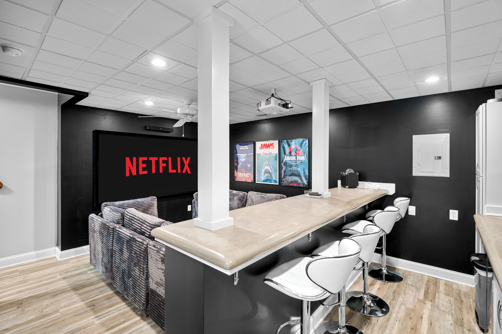 Un espace bar moderne avec un long comptoir et des tabourets de bar, un mur noir orné du logo Netflix et des affiches des films « Les Dents de la mer » et « Jurassic Park ».