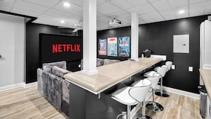 Ein moderner Barbereich mit einer langen Theke und Barhocker, einer schwarzen Wand mit Netflix-Branding sowie Postern von 'Jaws' und 'Jurassic Park'.