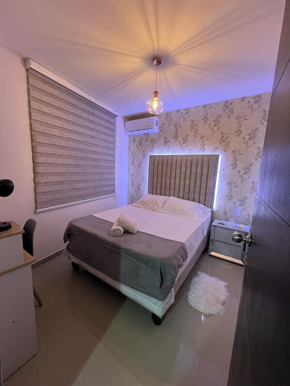 Un dormitorio con cama, mesita de noche, lámpara y una lámpara en el techo.