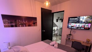 Ein Schlafzimmer mit Bett, Schreibtisch, Stuhl, Fernseher und einem Stadtbild.