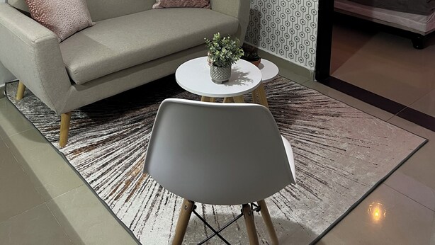 Ein modernes Wohnzimmer mit einer Couch, einem kleinen runden Tisch und einem Sessel. An der Wand hängt ein Bild und die Tapete hat ein Muster.