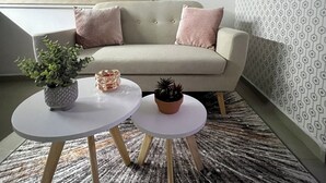 Ein Wohnzimmer mit einer Couch, zwei Beistelltischen, einer Zimmerpflanze und einem Bild an der Wand.