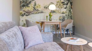 Ein Wohnzimmer mit einer Couch, einem runden Tisch mit Stühlen, einer Lampe und einem Bücherregal.