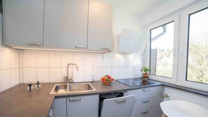 Eine moderne Küche mit weißen Schränken, einer Spüle aus Edelstahl und einem Fenster, das für natürliches Licht sorgt.