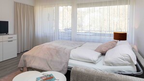 Ein Hotelzimmer mit Bett, Schreibtisch, Stuhl, Lampe und einem fenster mit Vorhängen.