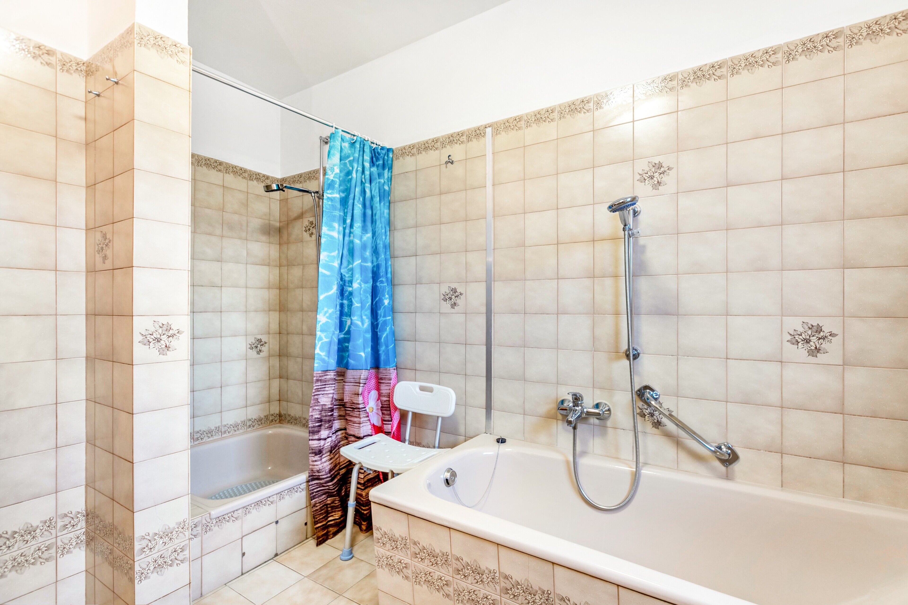 Une salle de bain avec une baignoire, une douche et une petite chaise blanche.